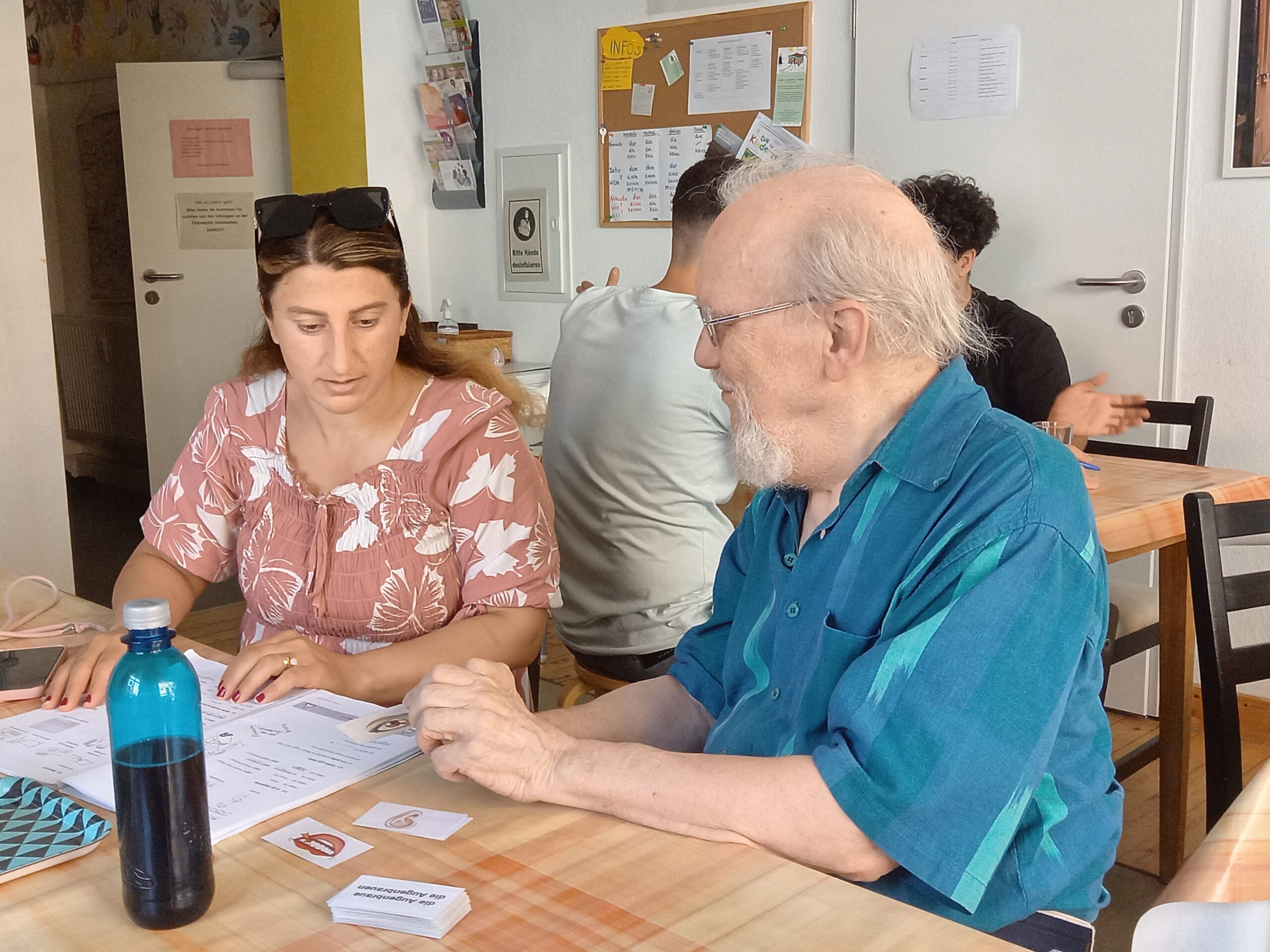 Frau und älterer Herr sitzen zusammen an einem Tisch und üben Deutsch