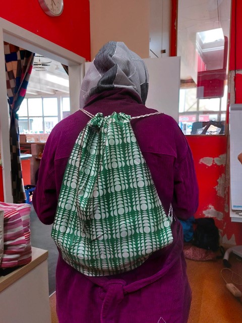 Frau mit Kopftuch steht mit dem Rücken zur Kamera und trägt einen selbstgenähten Rucksack