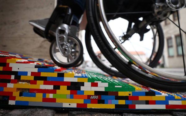 Ein Rollstuhlfahrer fährt eine Rampe aus bunten Legosteinen hoch.